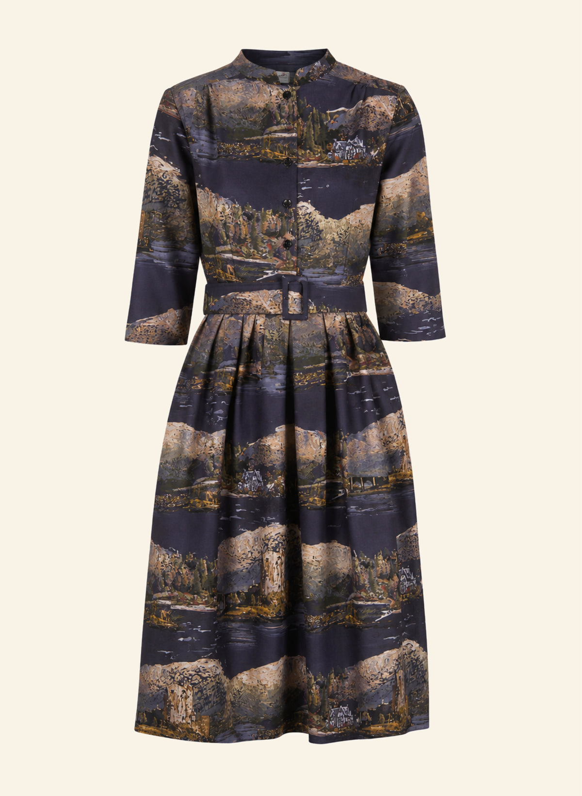 A long-sleeved midi dress with a button-up front and a pleated waist, featuring an all-over scenic landscape print in dark navy blue, beige, and brown tones, shown against a solid cream background.