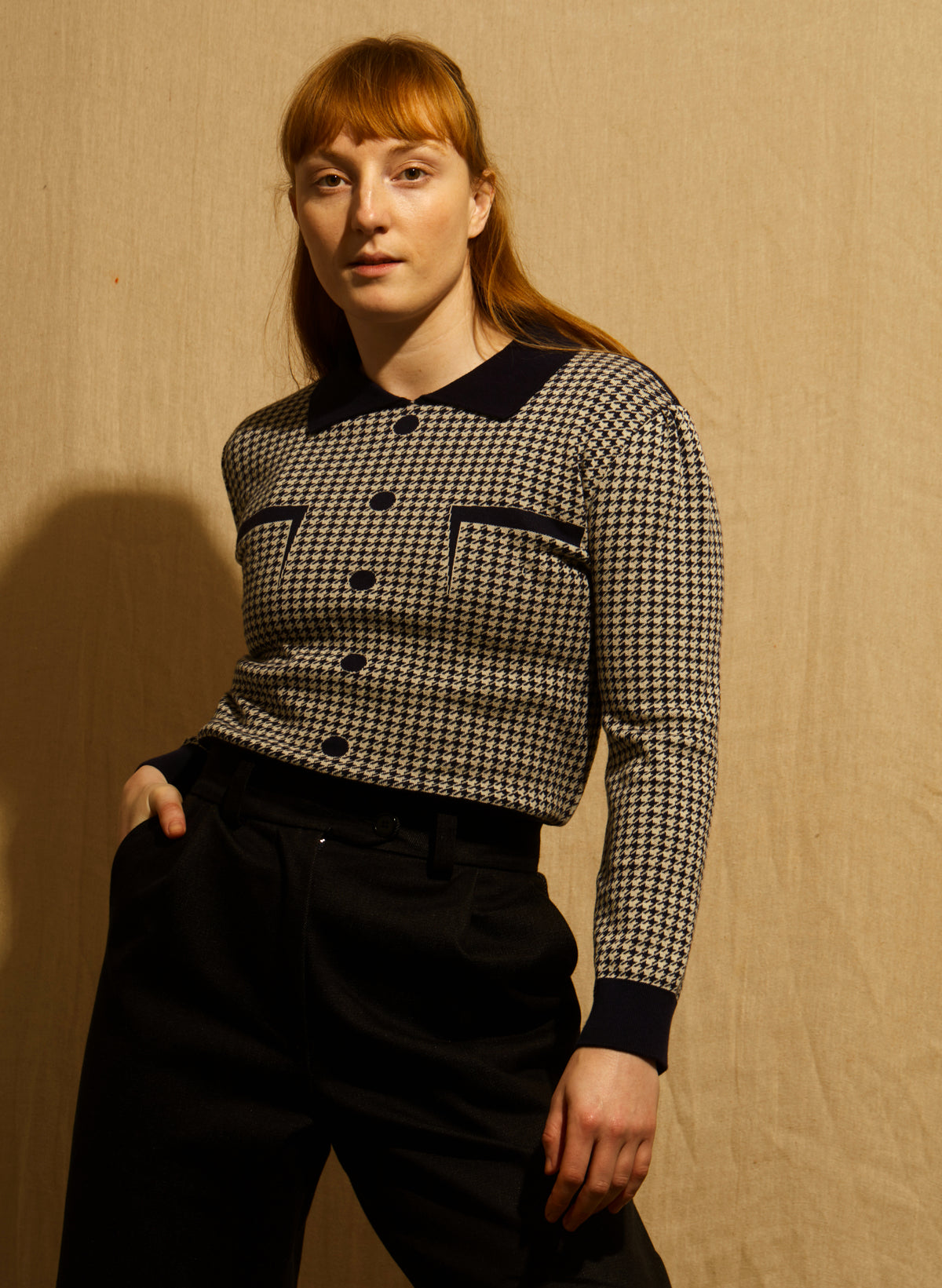 A women wearing a navy and beige houndstooth jacket with dark navy blue trim on the collar, cuffs, hem, and button details, and navy trousers, shown against a wooden background.