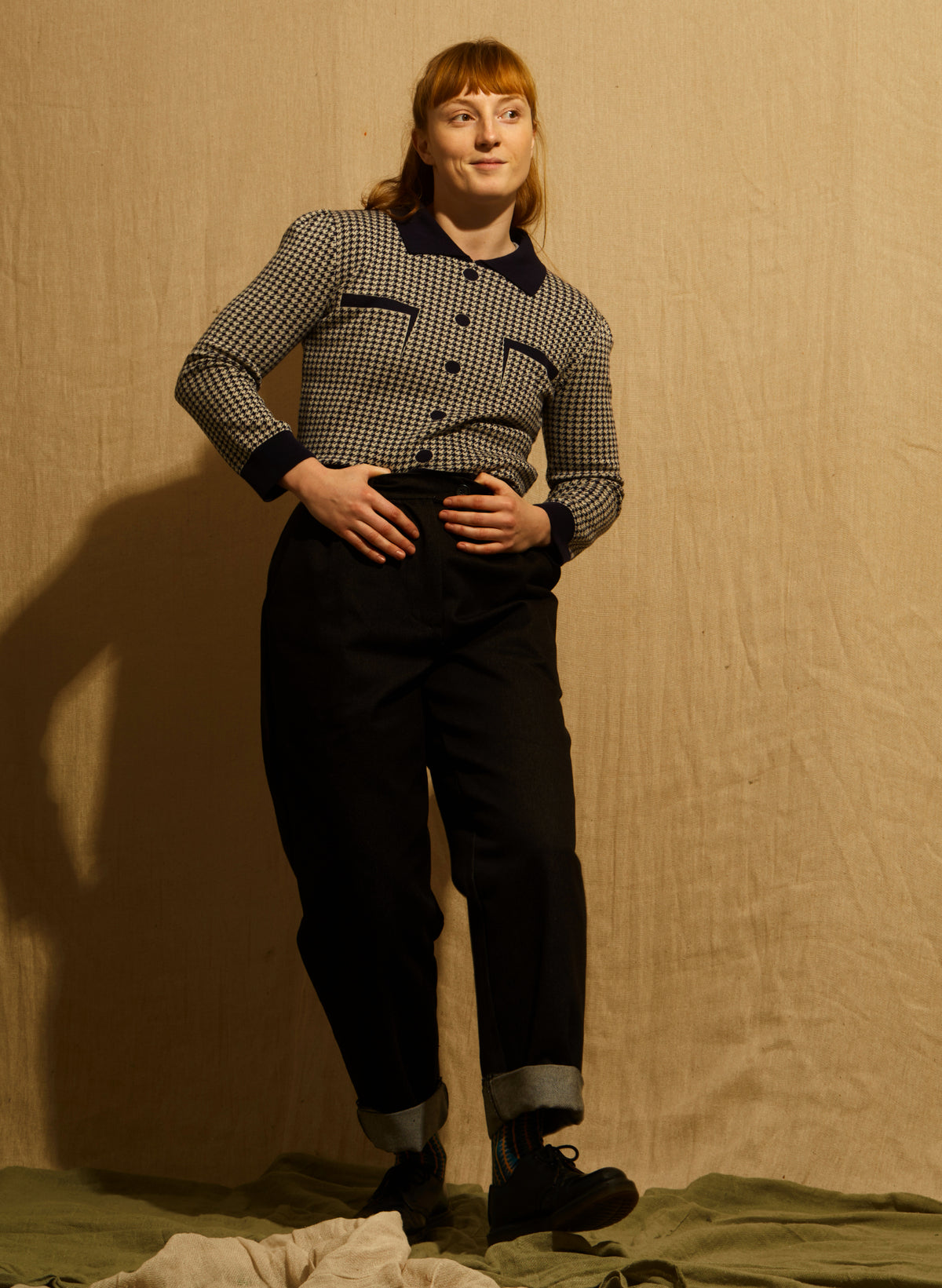 A women wearing a navy and beige houndstooth jacket with dark navy blue trim on the collar, cuffs, hem, and button details, and navy trousers, shown against a wooden background.